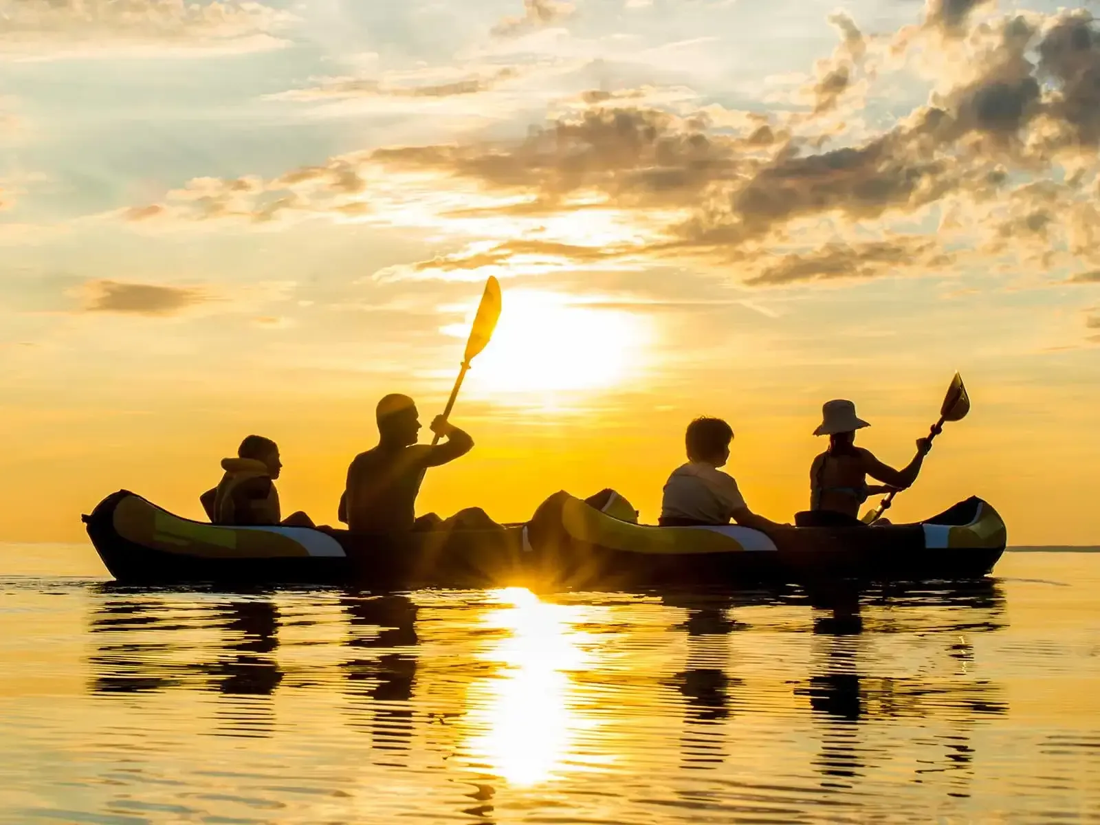 Eine Gruppe von Menschen paddelt auf dem Wasser, während Sonnenuntergang.