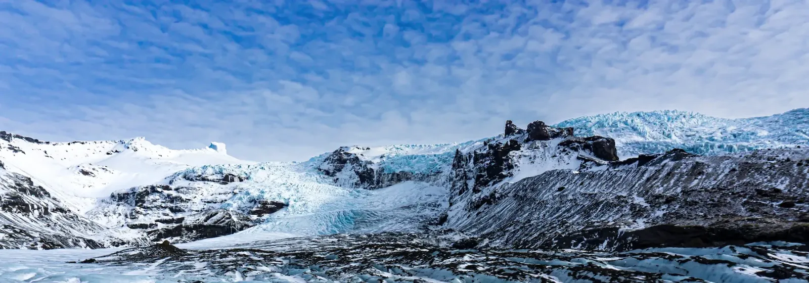 Skatafell Gletscher mit blauen Eisformationen und schneebedeckten Bergen unter einem klaren Himmel.