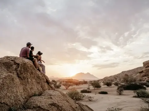 Drei Reisende bestaunen auf einem Felsen den Sonnenuntergang.