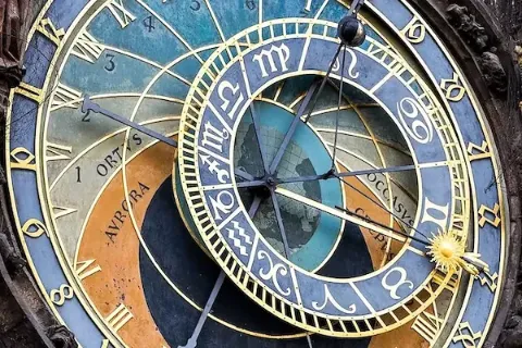 Detailansicht einer astronomischen Uhr mit goldenen Ziffern, farbigen Zifferblättern und einem Sonnensymbol.
