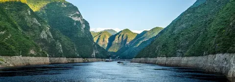 Breiter Fluss Yangzi zwischen bewaldeten Berghängen mit mehreren Booten auf dem Wasser.