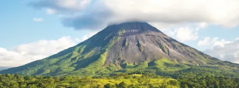 Der Vulkan Arenal inmitten von einer grünen Landschaft und blauem Himmel