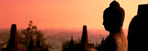 Buddha-Statue im Vordergrund vor mehreren Tempelstupas bei Sonnenaufgang.