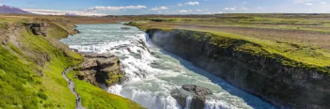 Gullfoss Wasserfall in Island, umgeben von üppiger grüner Landschaft und klarem blauen Himmel.