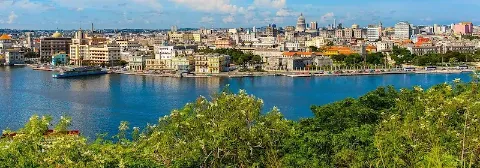Panoramablick auf die Stadt Havanna mit vielen Häusern vor dem blauen Meer und grünen Büschen.