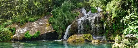 El Nicho Wasserfall im Naturpark Topes de Collantes fließt über moosbedeckte Felsen in ein klares Naturbecken.