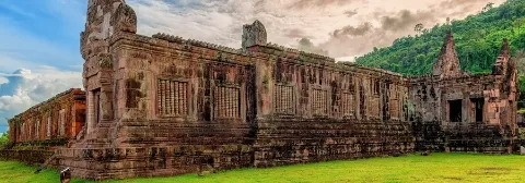 Hinduistischer Tempel Wat Phou in Laos steht auf einer grünen Wiese mit Bäumen im Hintergrund.