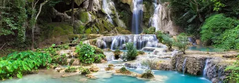 Kaskade des Kuang Si Wasserfall mit türkisblauem Wasser im grünen, tropischen Regenwald.