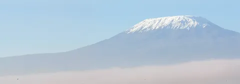Der schneebedeckte Berg Kilimandscharo erhebt sich über einem Wolkenmeer unter strahlend blauem Himmel.
