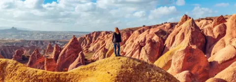 Frau steht auf einem Hügel und blickt auf die orangefarbenen Felsformationen in der Landschaft von Kappadokien.