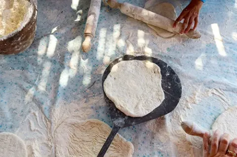 Das Bild ist von oben aufgenommen und zeigt einen Tisch, auf dem mehrere Hände gerade dabei sind, mit Nudelhölzern einen Teig auszurollen.