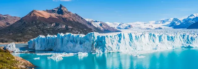 Panorama vom Perito-Moreno-Gletscher mit türkisblauem See im Vordergrund unter wolkenlosem Himmel.