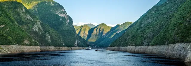 Breiter Fluss Yangzi zwischen bewaldeten Berghängen mit mehreren Booten auf dem Wasser.