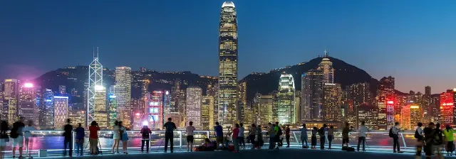 Menschen stehen vor der leuchtenden Skyline von Hongkong am Hafen bei Abenddämmerung.