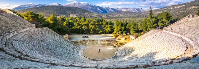 Das antike Theater von Epidaurus in Griechenland, umgeben von Bergen und Bäumen unter blauem Himmel.