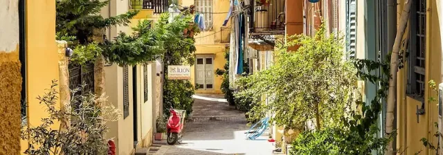 Eine sonnige Gasse in der Altstadt von Nauplia mit bunten Häusern, Pflanzen und einem roten Roller.
