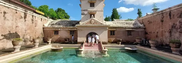 Hof vom Wasserschloss Tamansari mit klarem Wasserbecken und Brunnen unter blauem Himmel.