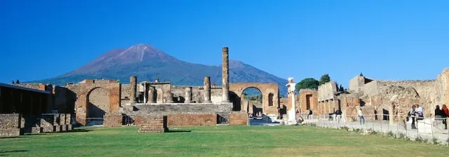 Die Ausgrabungsstätte von Pompeji mit dem Vulkan Vesuv im Hintergrund unter blauem Himmel.