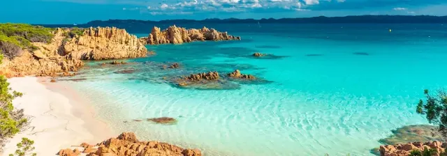 Bucht auf der Insel Budelli mit türkisblauem Wasser, braunen Felsen und weißem Sandstrand und blauem Himmel.