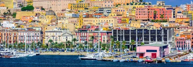 Blick auf die Stadt Cagliari auf Sardinien vom Meer aus mit Hafen und bunten Häusern.