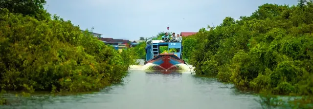 Boot mit Personen fährt über das Wasser eines Flusses mit grüner Vegetation am Ufer