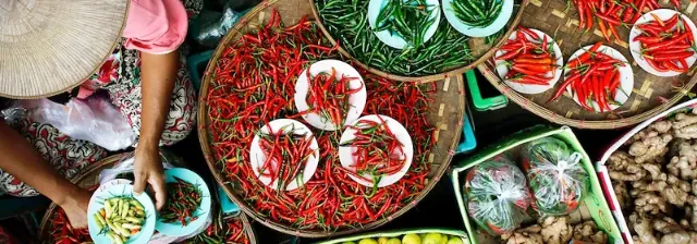 Marktszene in Laos von oben, bei der ein Händler roten und grünen Chilischoten, Gewürzen und Ingwer sortiert.