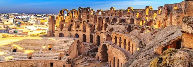 Teilansicht des antiken Amphitheaters in El Djem mit mehreren Rundbögen und Sitzreihen unter blauem Himmel.