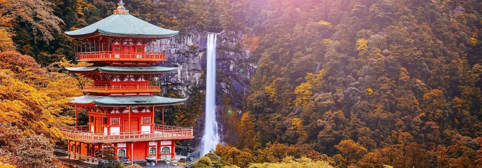 Tempel in Japan umgeben von bunten Herbstblättern und dem Nachi-Wasserfall im Hintergrund.