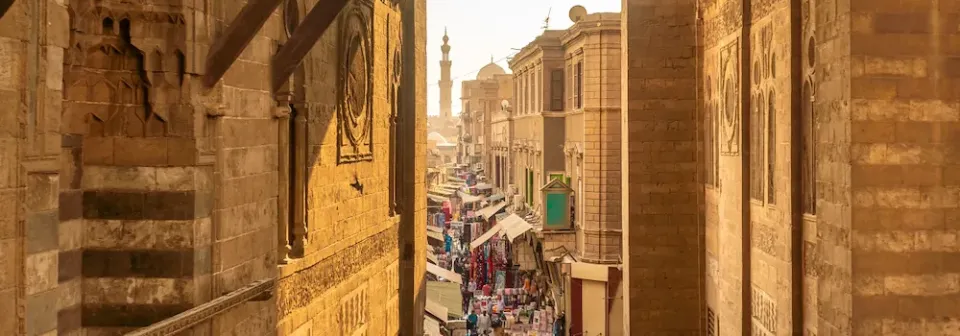Blick auf einen belebten Markt in Kairo, umgeben von historischen Gebäuden bei einer goldenen Abendstimmung.