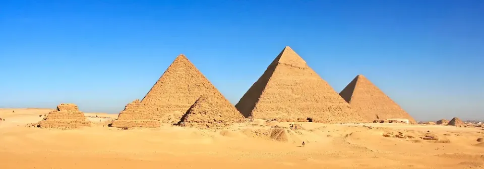 Pyramiden von Gizeh stehen in einer Wüstenlandschaft unter klarem blauen Himmel.