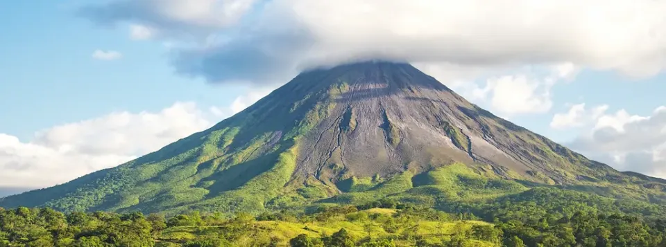 Der Vulkan Arenal inmitten von einer grünen Landschaft und blauem Himmel