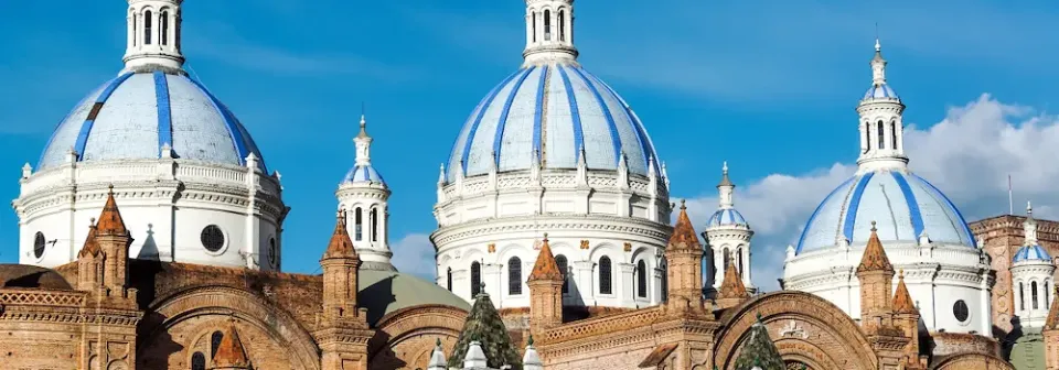 Drei Kuppeln mit blauen und weißen Streifen von der Kathedrale in Cuenca ragen über einer Backsteinfassade auf.