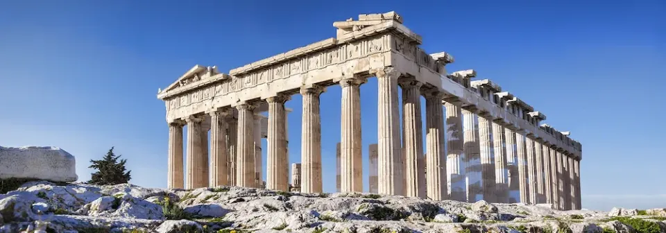 Antiker Parthenon-Tempel mit mehreren Säulen auf einem Hügel über Athen unter blauem Himmel.