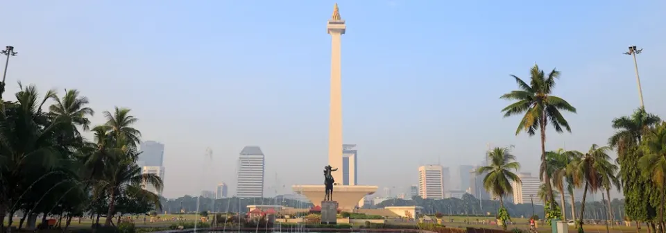 Das Nationaldenkmal Indonesiens Monas inmitten eines weitläufigen öffentlichen Parks unter blauem Himmel.