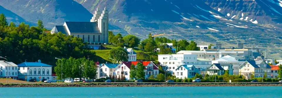 Panoramaaufnahme der Stadt Akureyri an der Küste mit bunten Häusern, einer Kirche und Bergen.