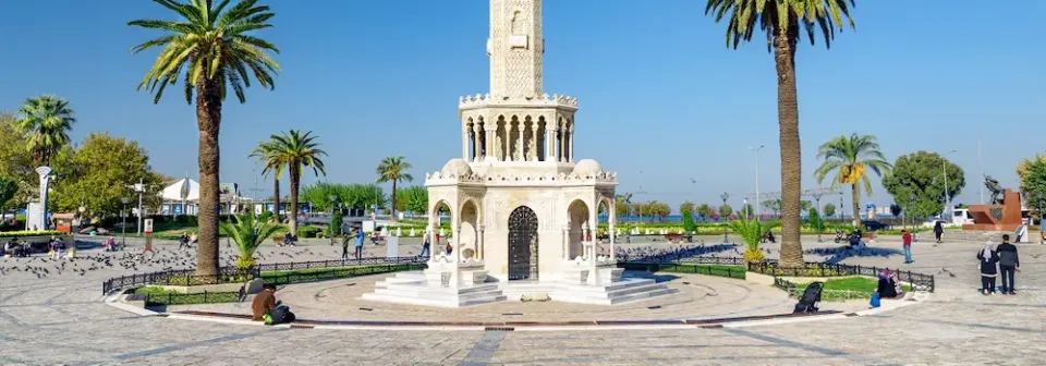 Historischer Uhrturm in Izmir mit filigranen Bögen auf dem weitläufigen Konak-Platz mit Palmen und Sitzbänken.