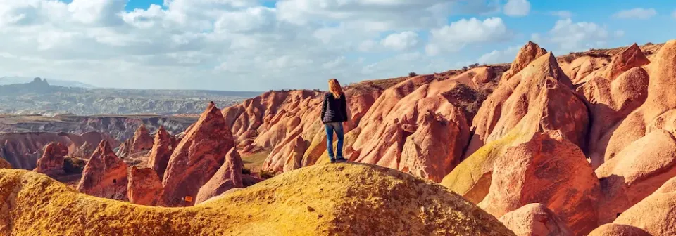 Frau steht auf einem Hügel und blickt auf die orangefarbenen Felsformationen in der Landschaft von Kappadokien.