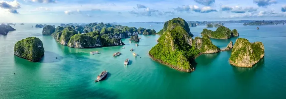 Luftaufnahme der Halong-Bucht mit Karststeinfelsen und Booten unter blauem Himmel