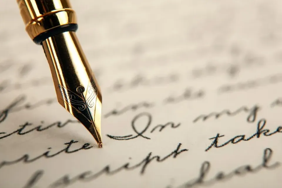 Nahaufnahme einer goldenen Schreibfeder und schwarzer Schrift.