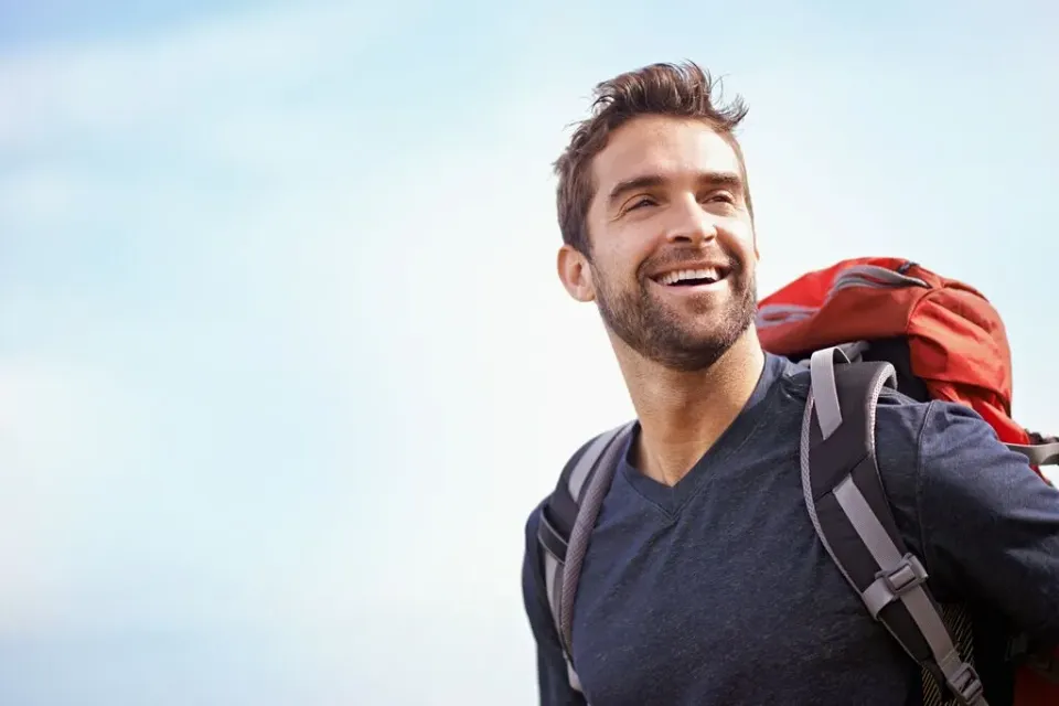 Portrait eines Mannes mit Rucksack, der lachend in die Ferne blickt.