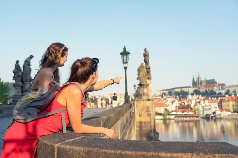 Zwei Frauen lehnen an einem Brückengeländer und zeigen auf ein Gebäude.