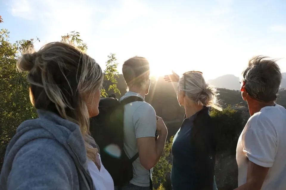 Zwei Frauen und zwei Männer stehen vor einem Bergpanorama und blicken gegen das Sonnenlicht auf die Gipfel.