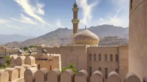 Auf Ihrer Reise durch den Oman sehen Sie den Turm des Forts, das höchste Gebäude in Nizwa. Der Blick schweift über die Neu- und die Altstadt, die Gärten und Lehmhäuser bis hinüber zu den Bergen.