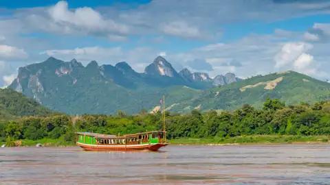 Bei unserer Reise empfängt uns unser laotischer Scout und nimmt uns mit auf ein traditionelles Mekongboot. Wir gleiten den mächtigen Strom hinab und betrachten die wilde grüne Landschaft an seinem Ufer.