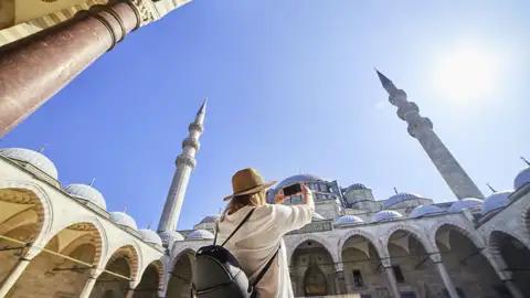 Eine Frau fotografiert während einer im Reiseverlauf inkludierten Besichtigung die beeindruckenden Kuppeln und Minarette der Blauen Moschee in Istanbul, ein Highlight dieser Top-Preis-Reise.