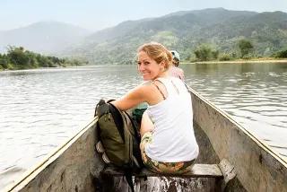 Eine lächelnde Frau im Kanu auf einem ruhigen Fluss mit Bergen im Hintergrund.