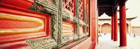 Detailansicht einer kunstvoll verzierten Wand mit roten Säulen in der Verbotenen Stadt in Peking.