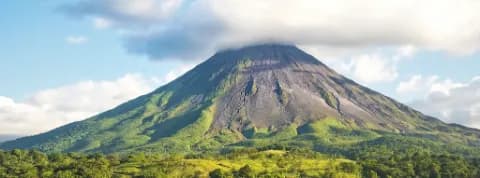 Der Vulkan Arenal inmitten von einer grünen Landschaft und blauem Himmel