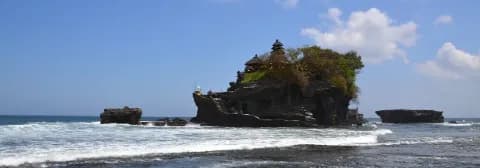 Tempel Pura Tanah Lot liegt auf einem Felsen mitten im Meer unter blauem Himmel.