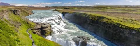 Gullfoss Wasserfall in Island, umgeben von üppiger grüner Landschaft und klarem blauen Himmel.
